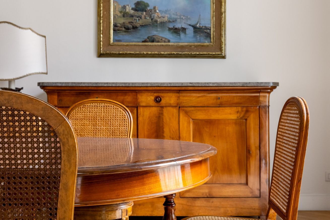 A dining area with a wooden table, wicker chairs, and a wooden cabinet.