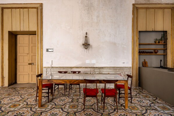 A dining area with a long table, red chairs, and a chandelier. - Sant'Isidoro Palace by DomuSicily (Palermo)