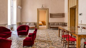 A spacious room with a large table and several red upholstered chairs. There are two sofas along the walls and a chandelier hanging from the ceiling.