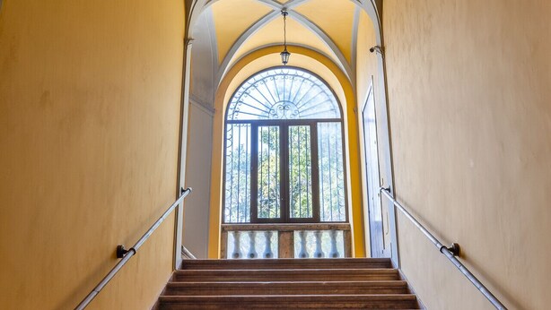 A staircase with wooden steps and metal railings, leading to a large arched window with a view of trees.
