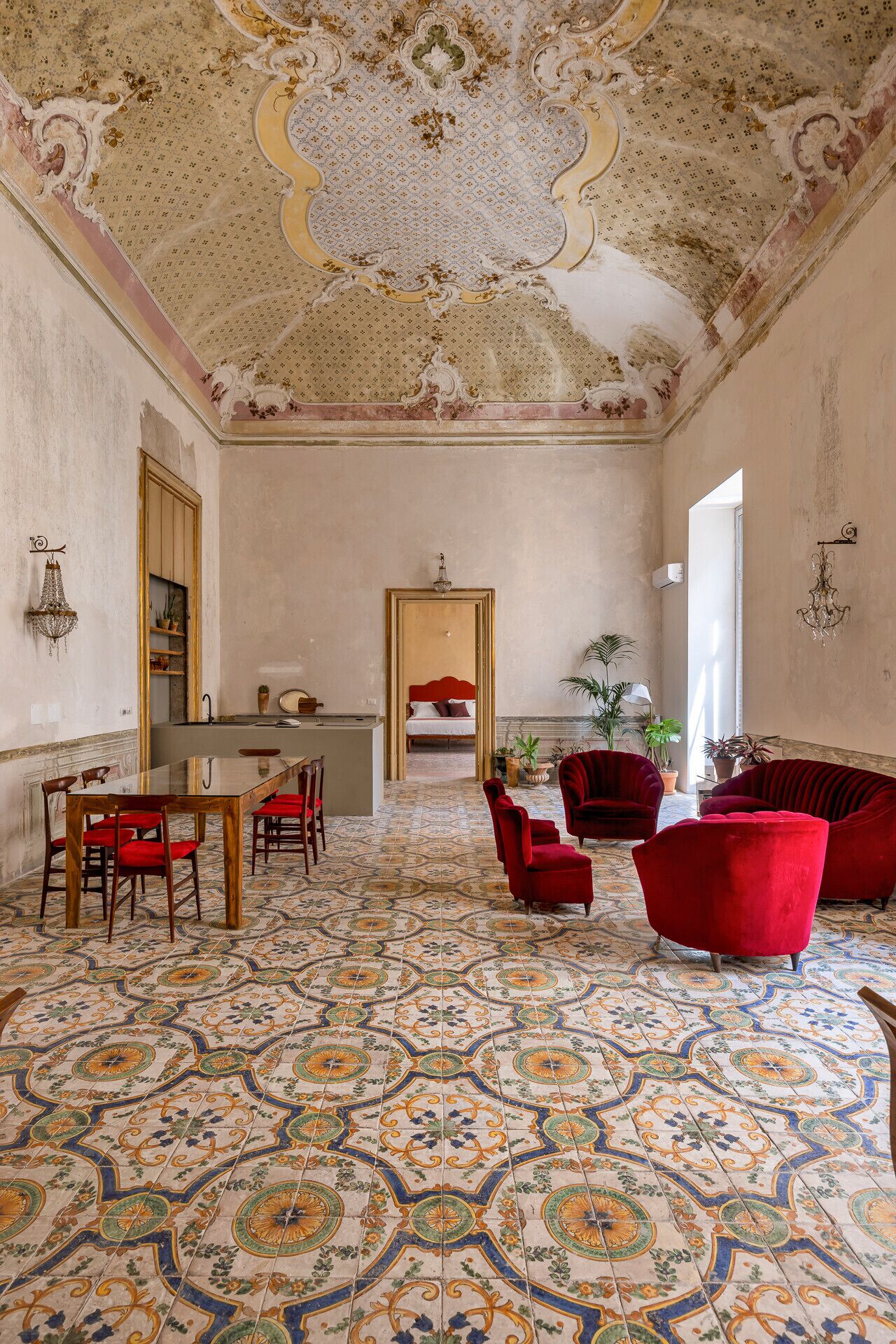 A spacious room with a patterned floor, a dining area with a table and chairs, and a seating area with red upholstered chairs.