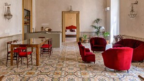 A spacious room with a patterned floor, a dining area with a table and chairs, and a seating area with red upholstered chairs.