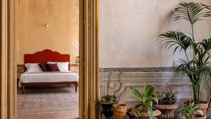 A room with a bed, a red headboard, and multiple potted plants.
