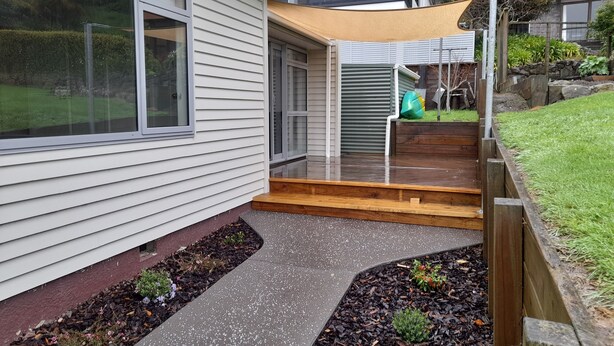 Une maison moderne dotée d’un patio couvert, d’un petit jardin et d’une terrasse en bois.