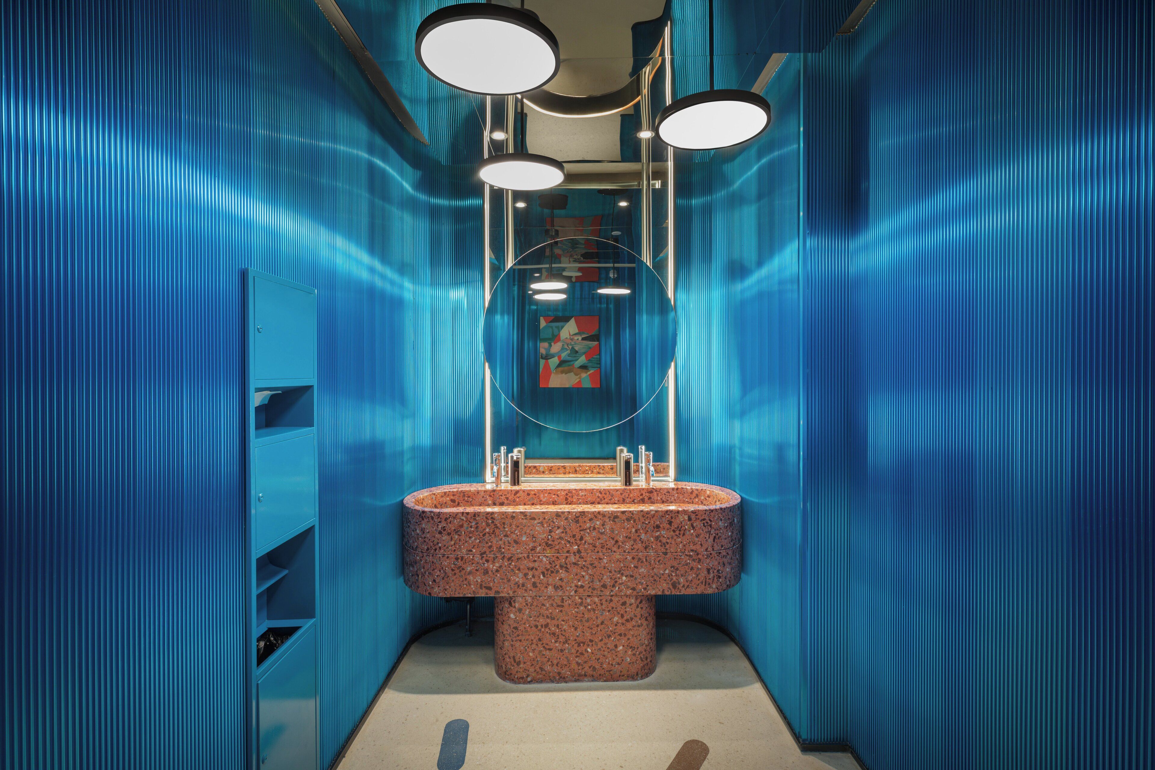 Een badkamer met een ruime granieten wastafel, blauwe wanden en drie ronde inbouwspots.