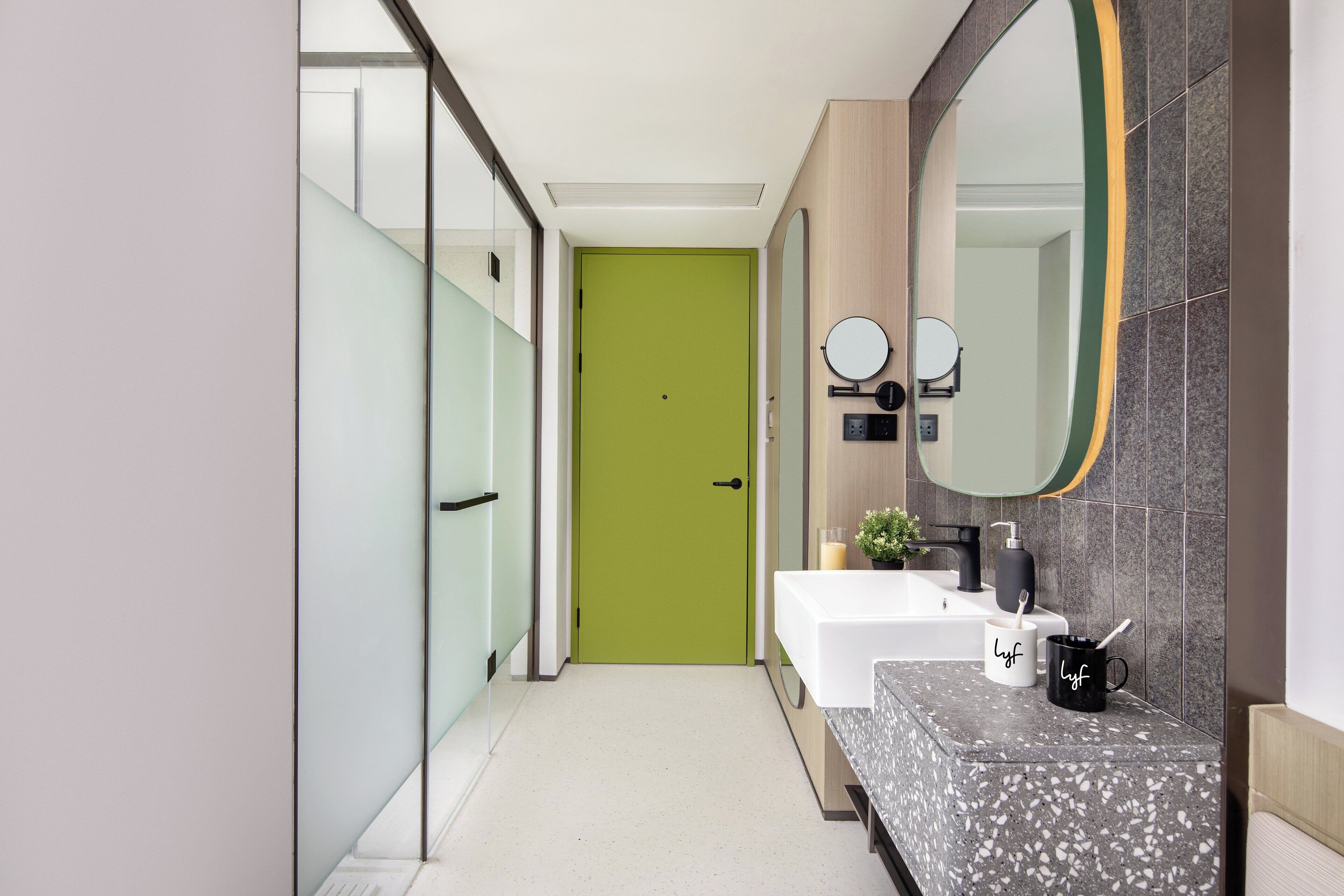 A modern bathroom with a green door, a white sink, a large mirror, and a marble countertop.