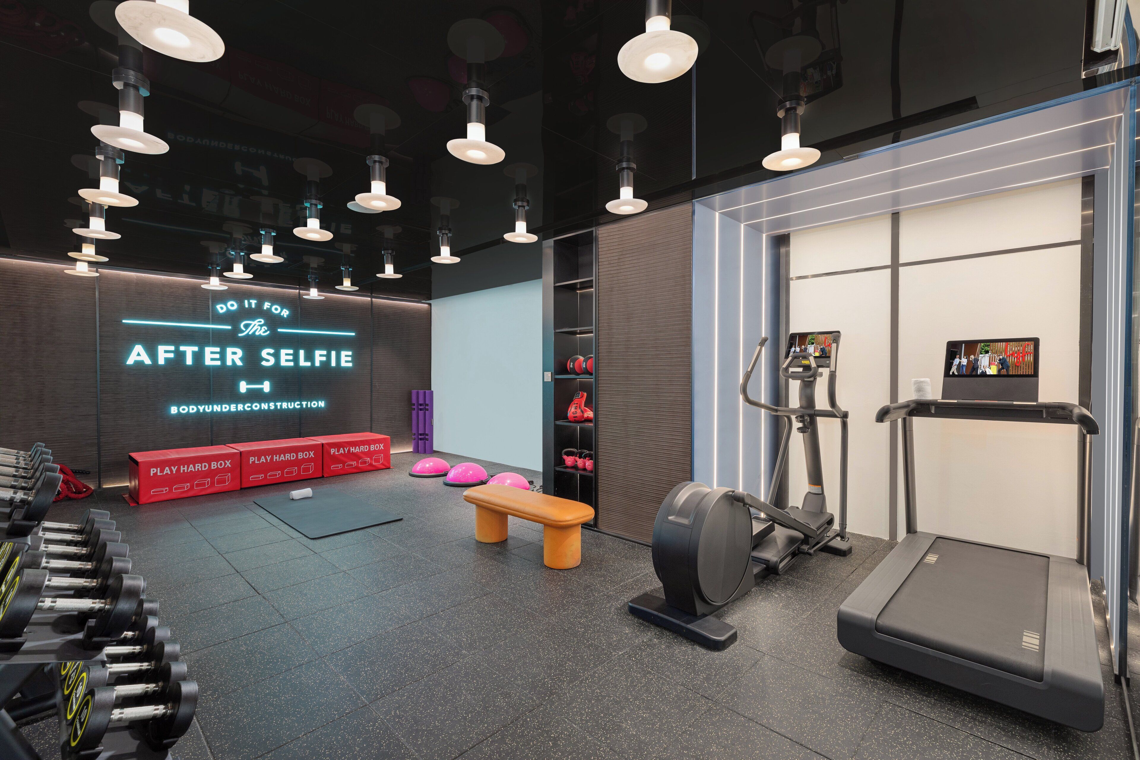 A modern gym with dumbbells, a bench, a treadmill, and a wall with motivational text.
