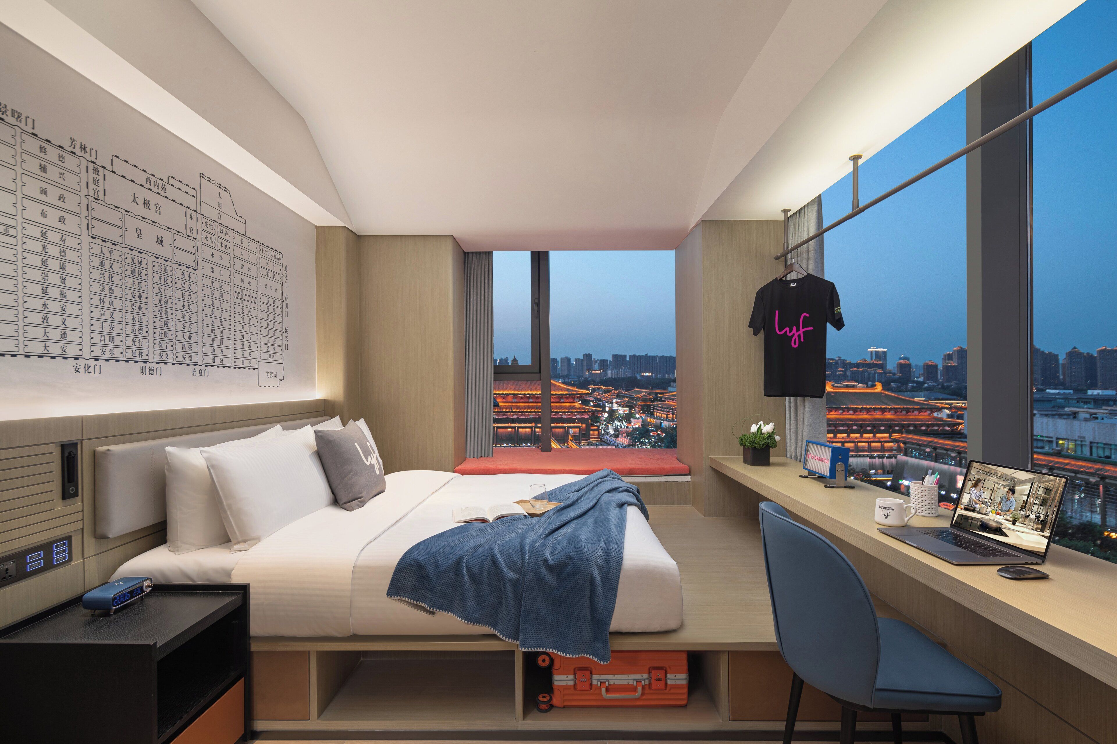 A modern hotel room with a large bed, a desk with a laptop, and a city view.