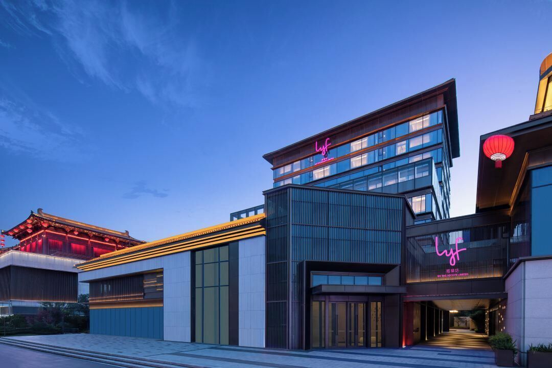 Un hôtel moderne, avec un élément d’architecture chinoise traditionnelle sur le côté gauche, une enseigne au néon et une lanterne rouge sur le côté droit.