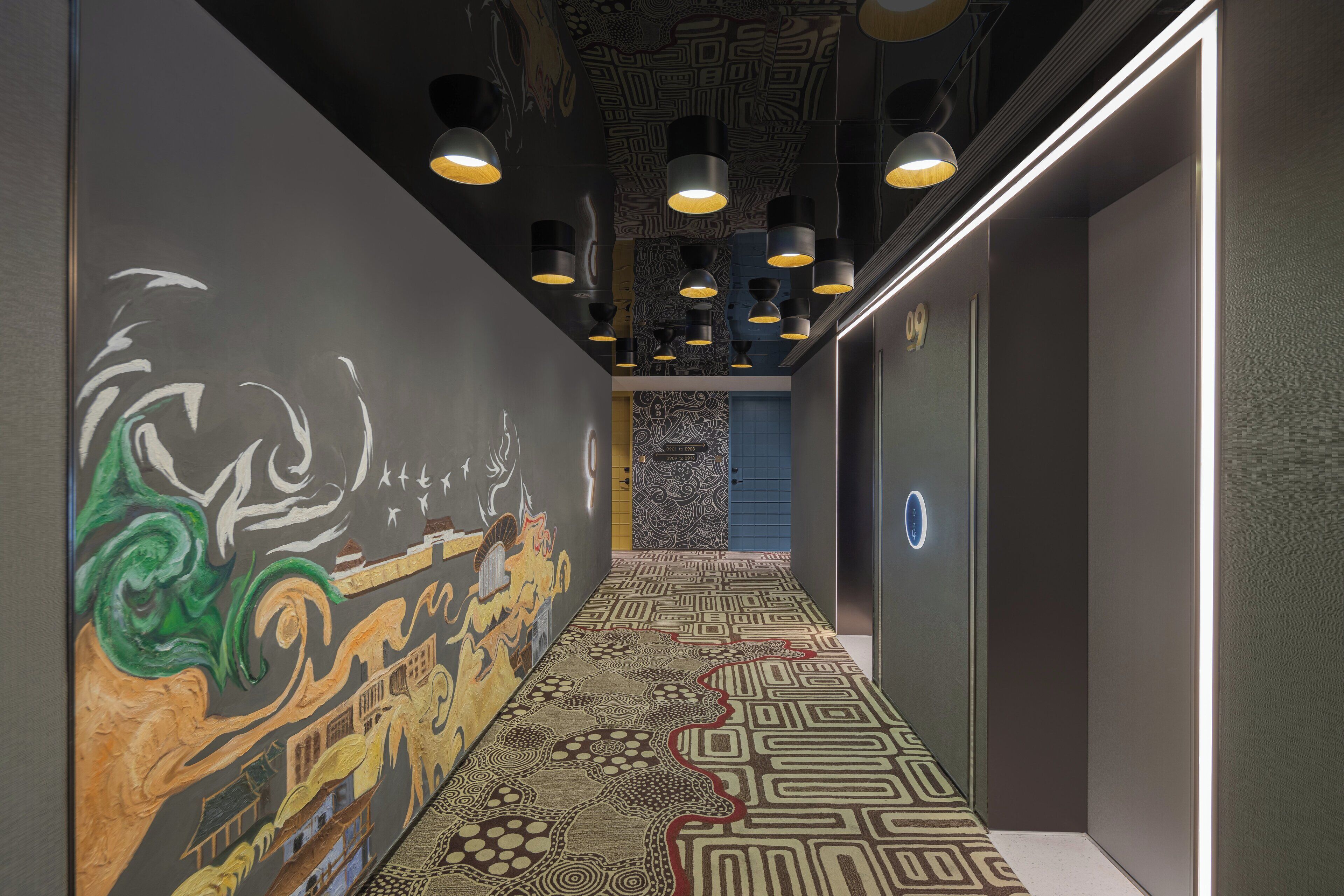 Un pasillo con alfombra estampada, obras de arte en la pared e iluminación colgante.
