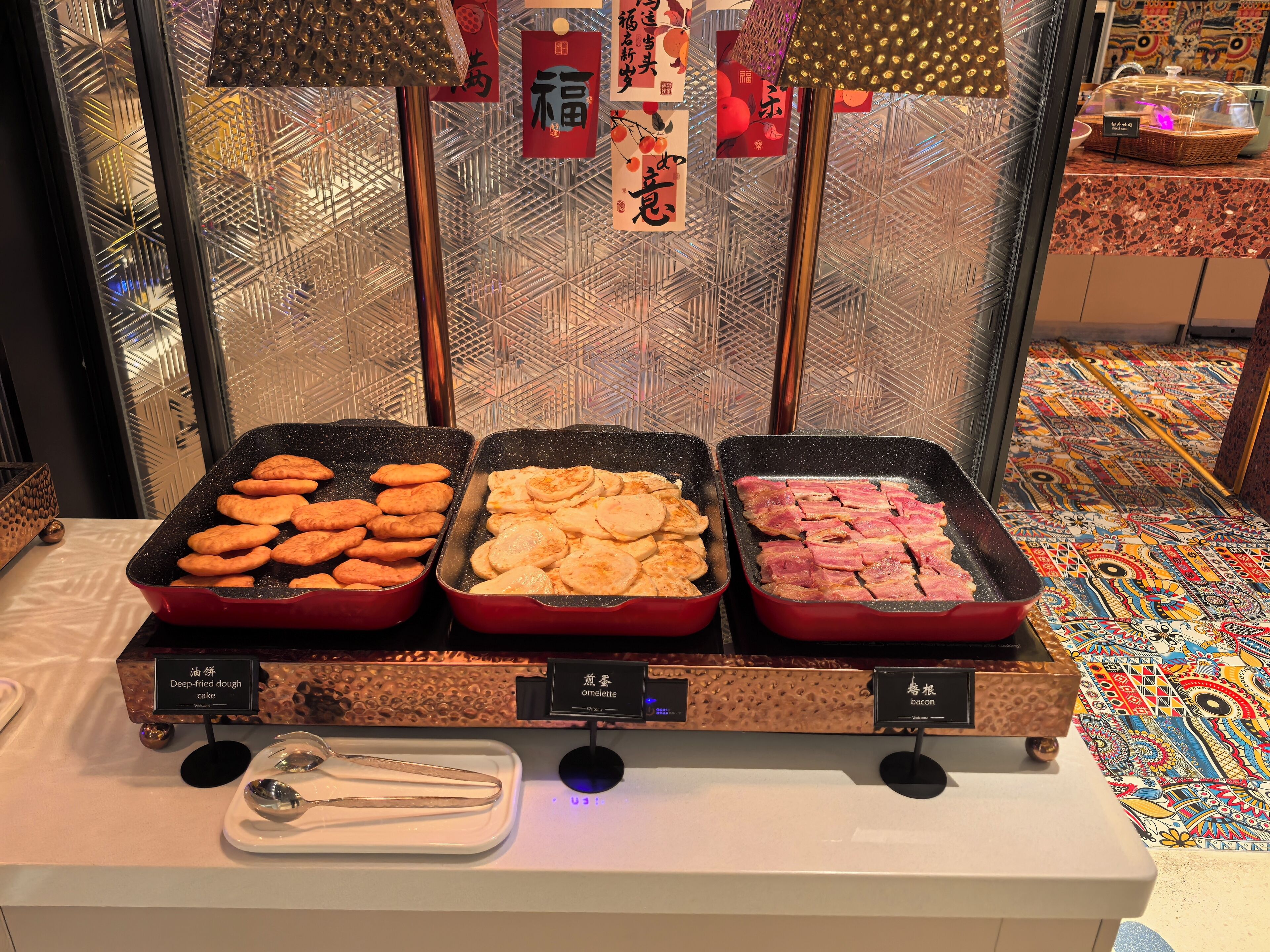 A buffet with trays of deep-fried dough cake, omelette, and bacon.