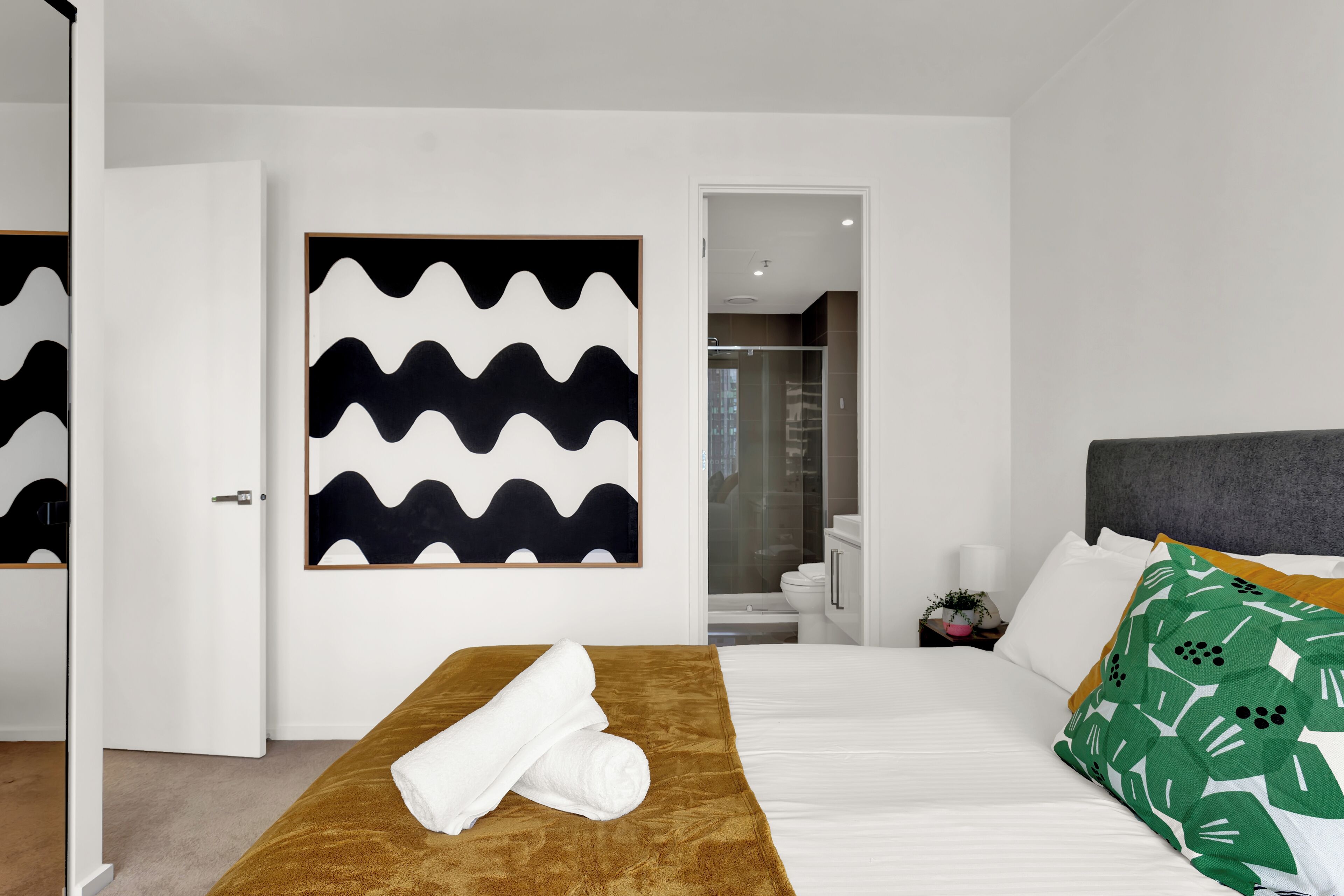 Een moderne hotelkamer met een opgemaakt bed, een bruin hoofdeinde en een groot abstract schilderij aan de muur.