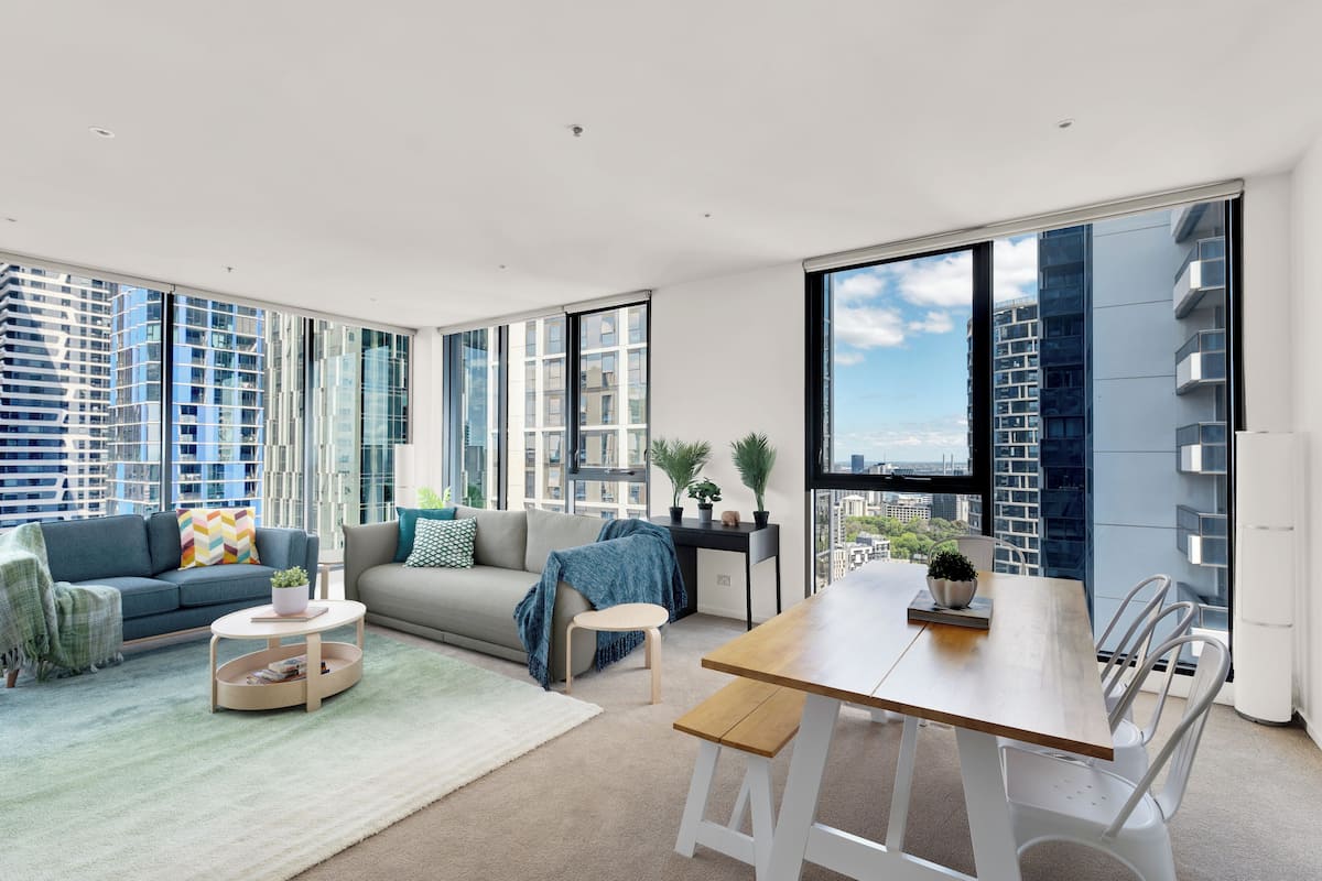 Un moderno salón con sofá, mesa de centro y comedor, con ventanas amplias que ofrecen vistas a la ciudad.