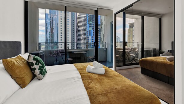 A modern hotel room with a large bed, a desk, and a balcony with a city view. - Nook Melbourne - Zen Apartments (Melbourne)