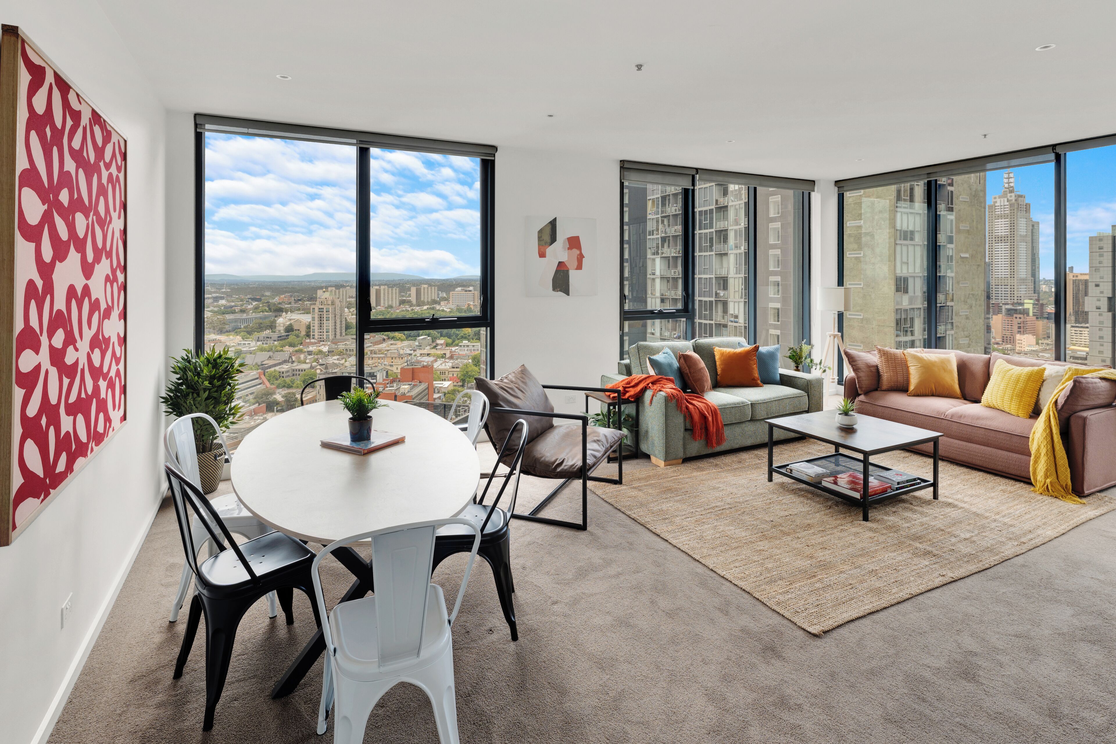 A modern living room with a dining area, large windows, and a city view.
