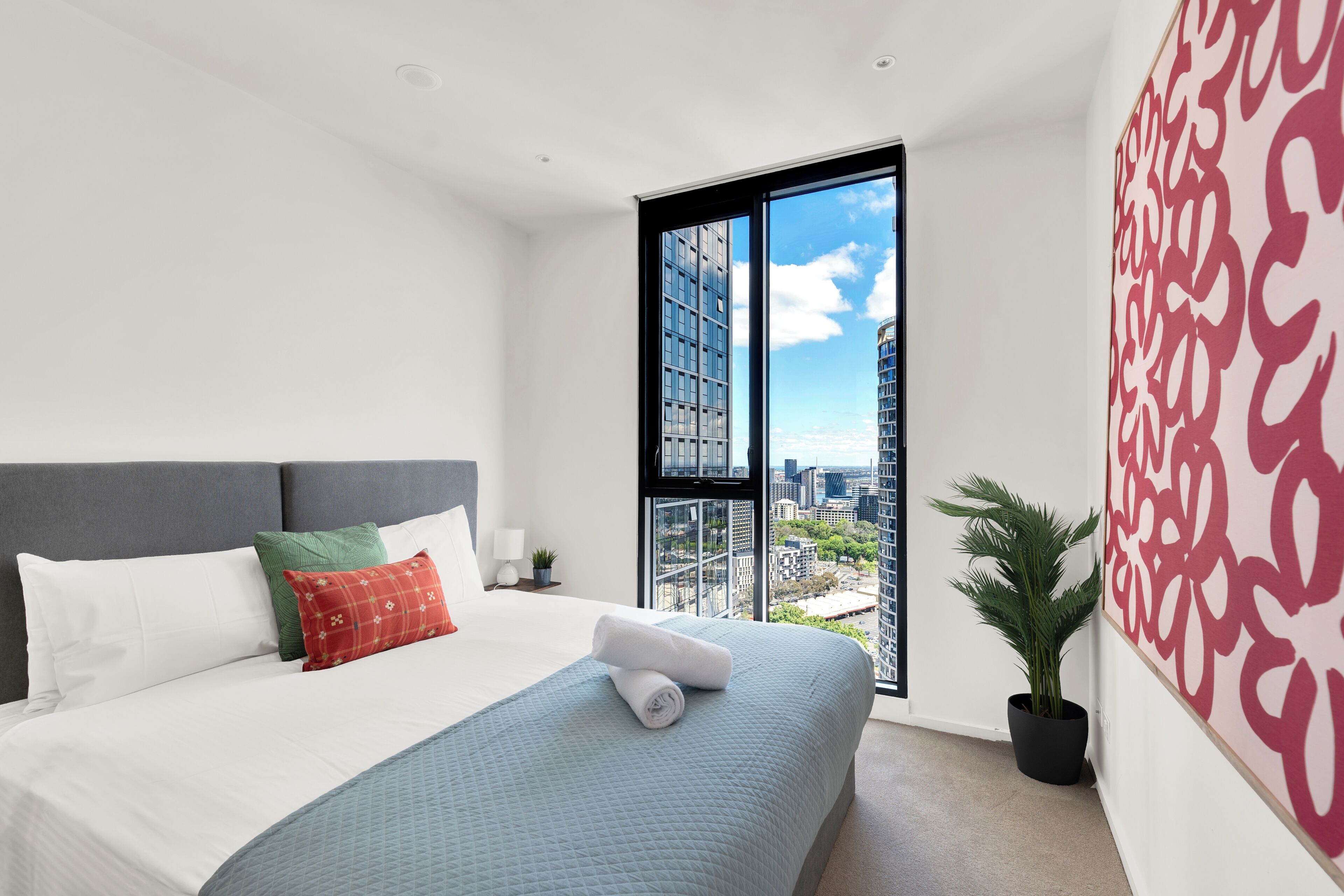 Une chambre d’hôtel moderne avec un grand lit, une vue sur la ville par une grande fenêtre et un élément décoratif mural.