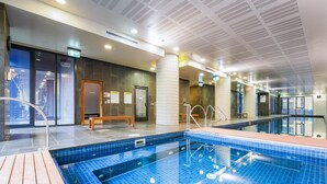 An indoor swimming pool with clear water, a wooden deck, and a sauna area visible through glass doors. - Nook Melbourne - Zen Apartments (Melbourne)