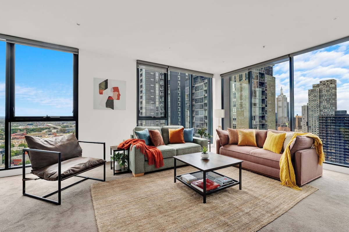 Una sala de estar moderna con un sofá, un sillón y una mesa de centro, ventanas amplias con vista a la ciudad y una obra de arte enmarcada en la pared.
