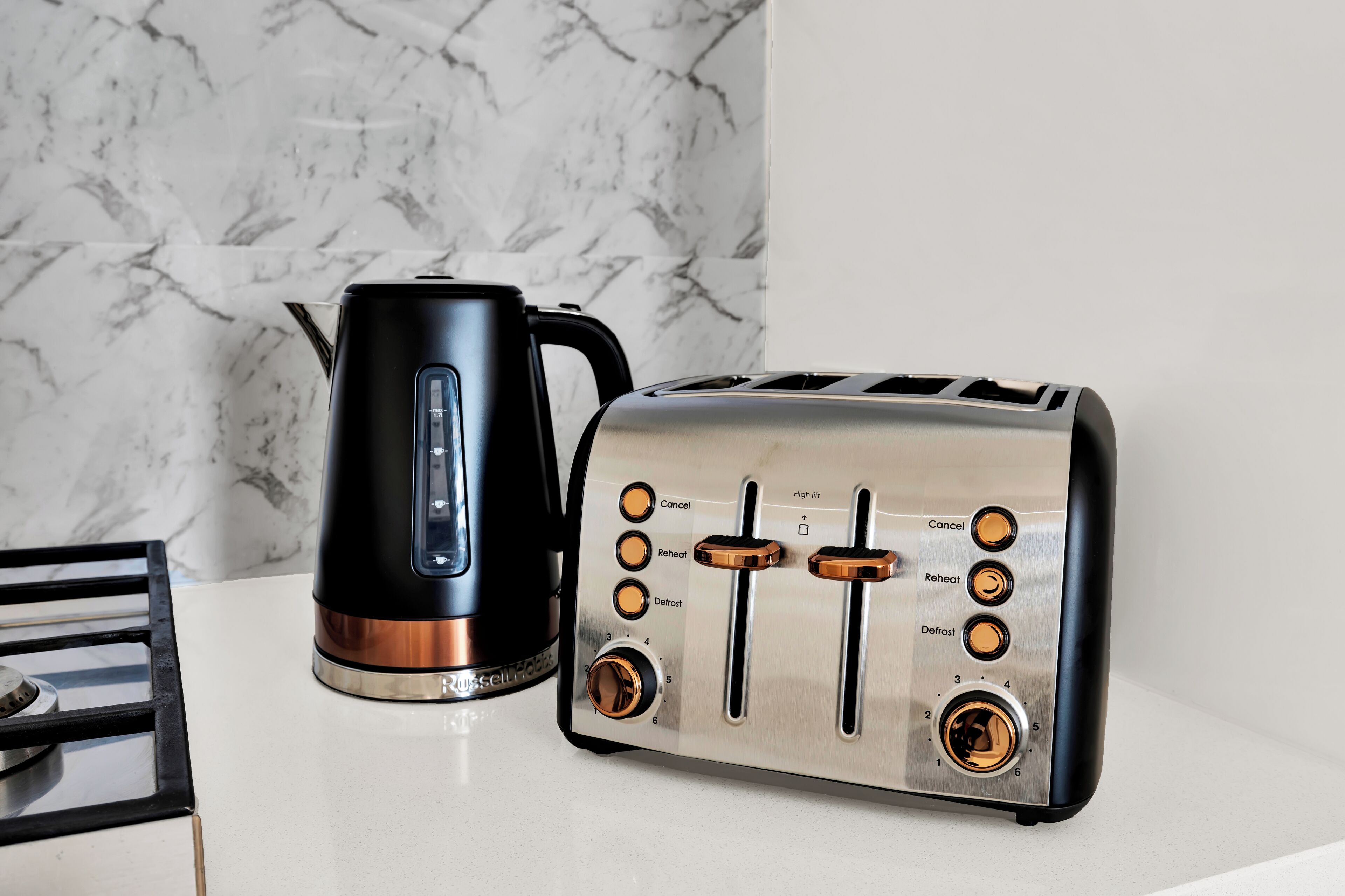 A kitchen with a black kettle and a stainless steel toaster on a white countertop.