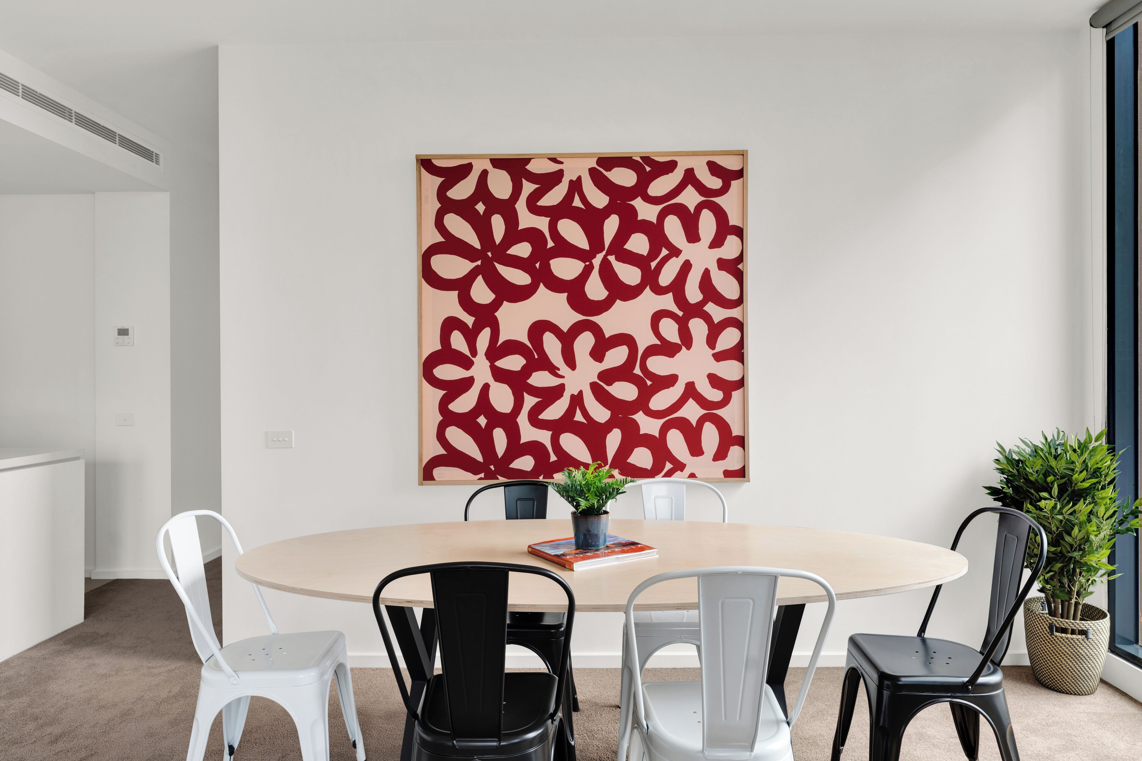 A conference room with a round table, six chairs, a potted plant, and a large abstract artwork on the wall.