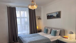 A bedroom with a bed, a nightstand, a lamp, a painting, and a window with curtains.