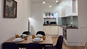 A dining area with a table set for four, a kitchen in the background, and a painting on the wall.