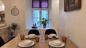 A dining area with a table set for four, a window with plants, and a painting on the wall.