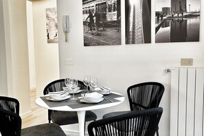 Een eethoek met een ronde tafel gedekt voor vier personen, zwarte stoelen en zwart-wit foto's aan de muur.