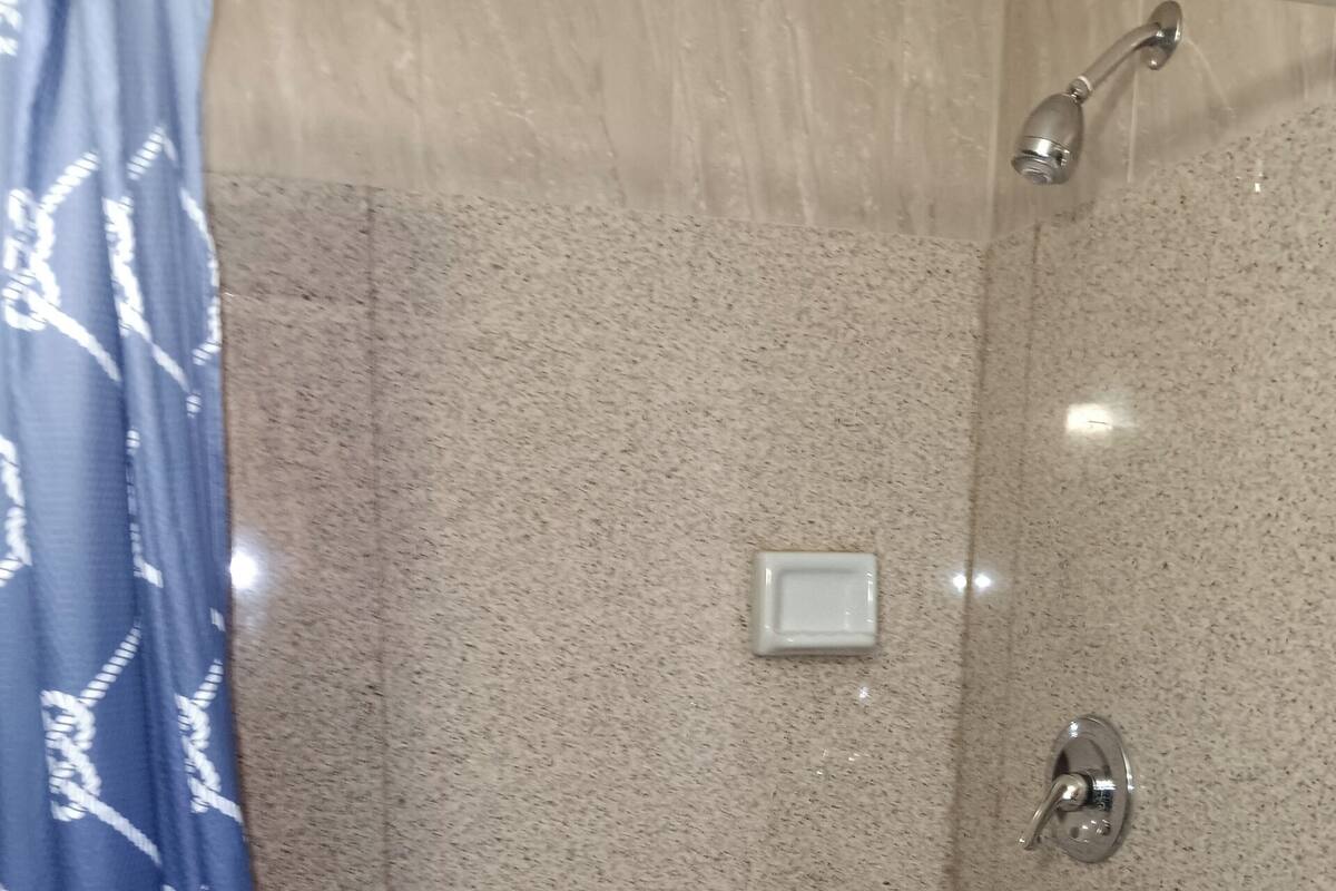 A shower area with a tiled floor, a showerhead, and a control panel.