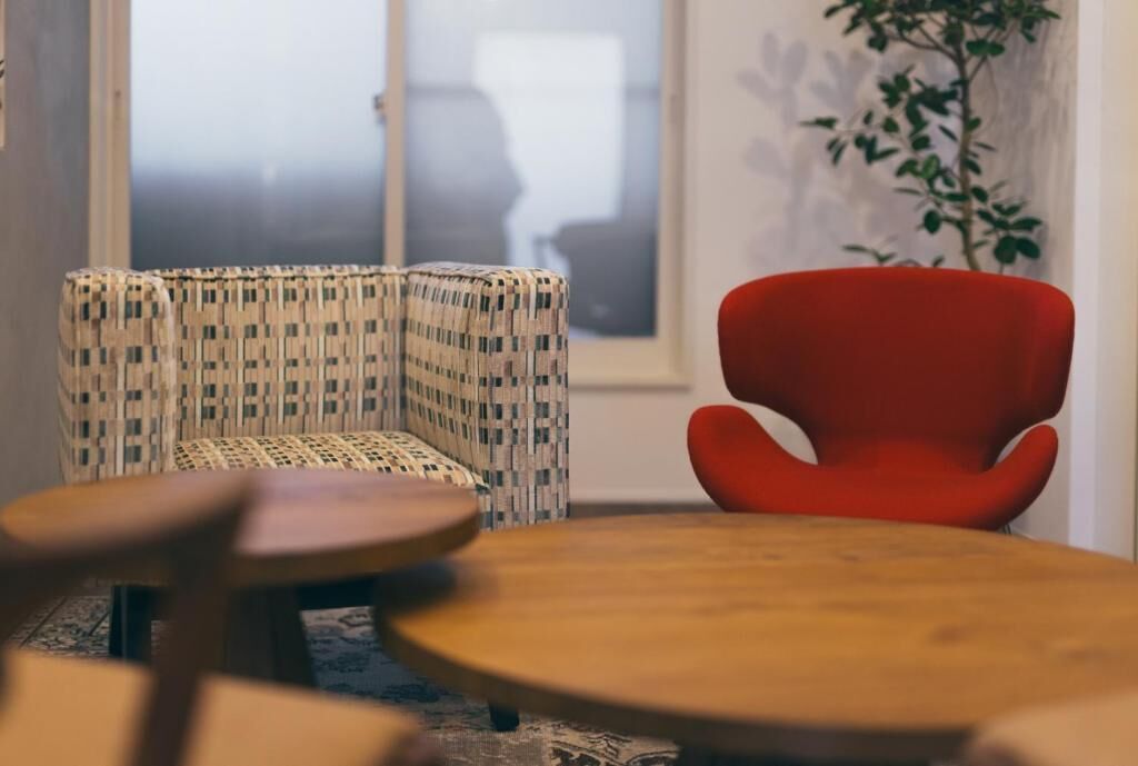 A room with a patterned sofa, a red chair, and a round wooden table.
