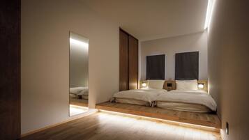 A modern bedroom with a large mirror, two beds with headboards, and a wooden floor.