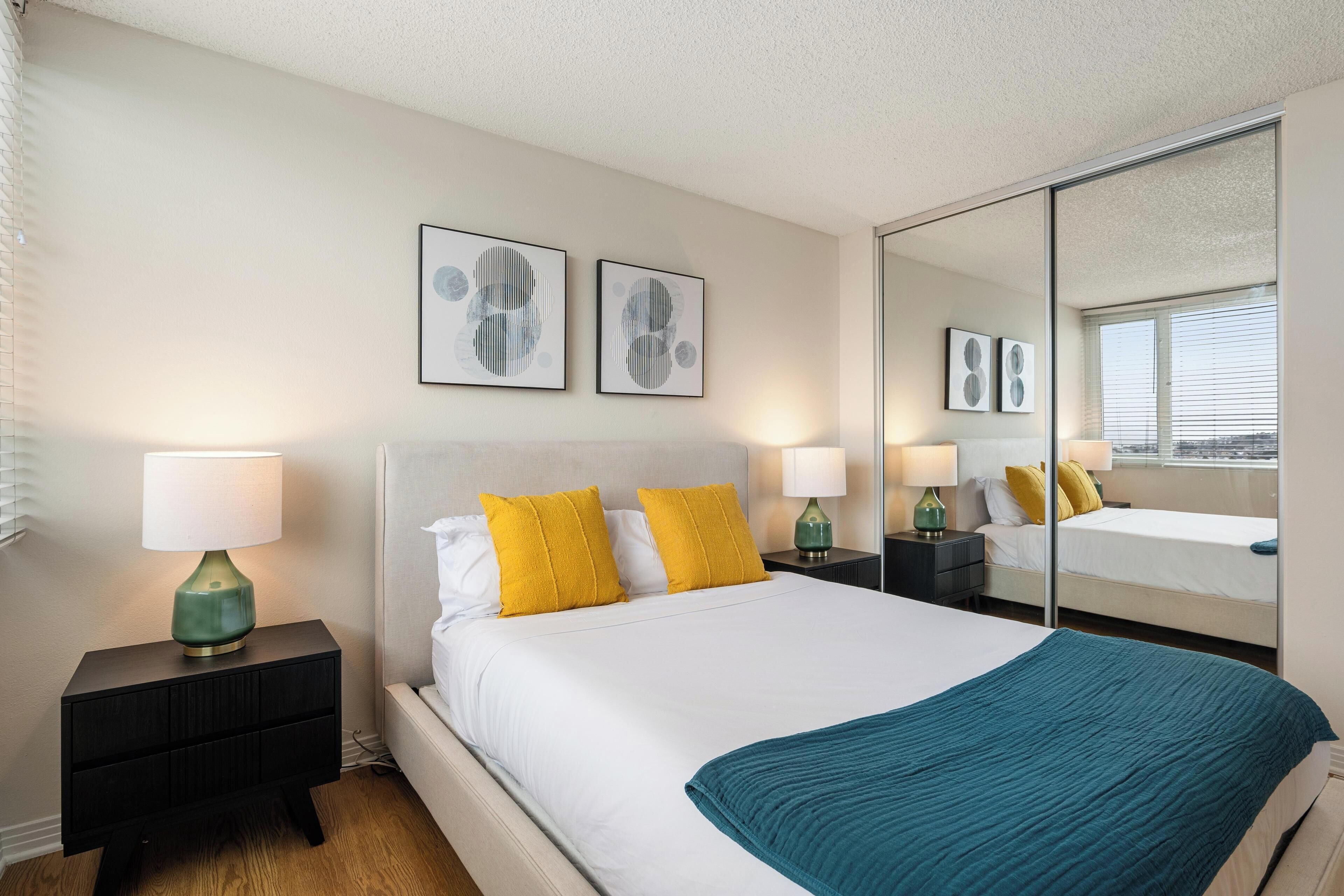 A neatly made bed with white bedding and a teal throw, flanked by two nightstands with lamps.