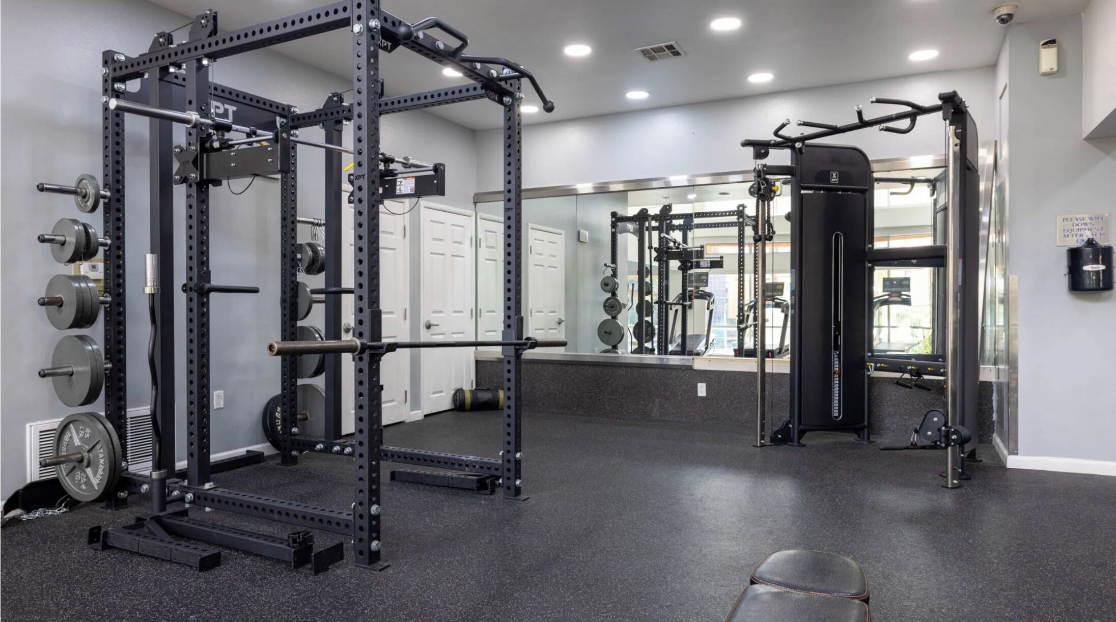 A gym with weightlifting equipment, treadmills, and a mirrored wall.