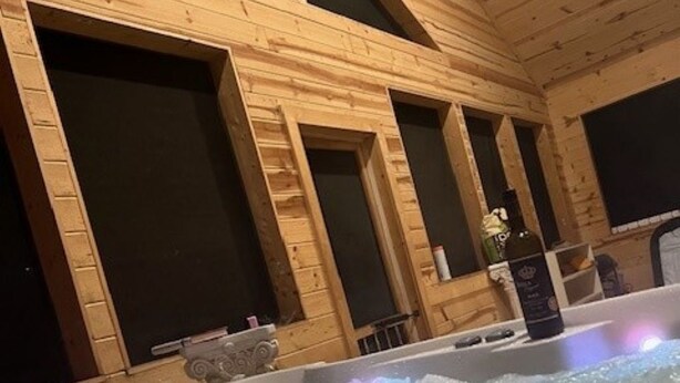 Interior de una cabaña de madera con jacuzzi y grandes ventanales.