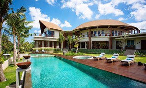 A modern resort with a large pool, lounge chairs, and a two-story building with a curved roof. - Umah Daun by Nakula (Kerobokan)
