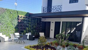 A modern building with a balcony, outdoor seating area, and a landscaped garden with various plants. - Casa Love Us (Tequisquiapan)