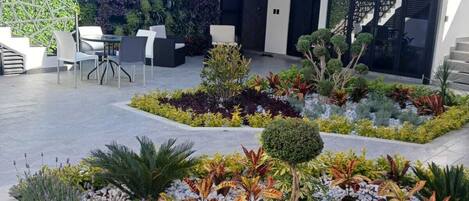 A modern building with a balcony, outdoor seating area, and a landscaped garden with various plants.