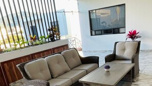 A wicker sofa set with cushions, a matching armchair, and a rectangular coffee table in a room with marble flooring and a balcony with a railing. - Casa Love Us (Tequisquiapan)