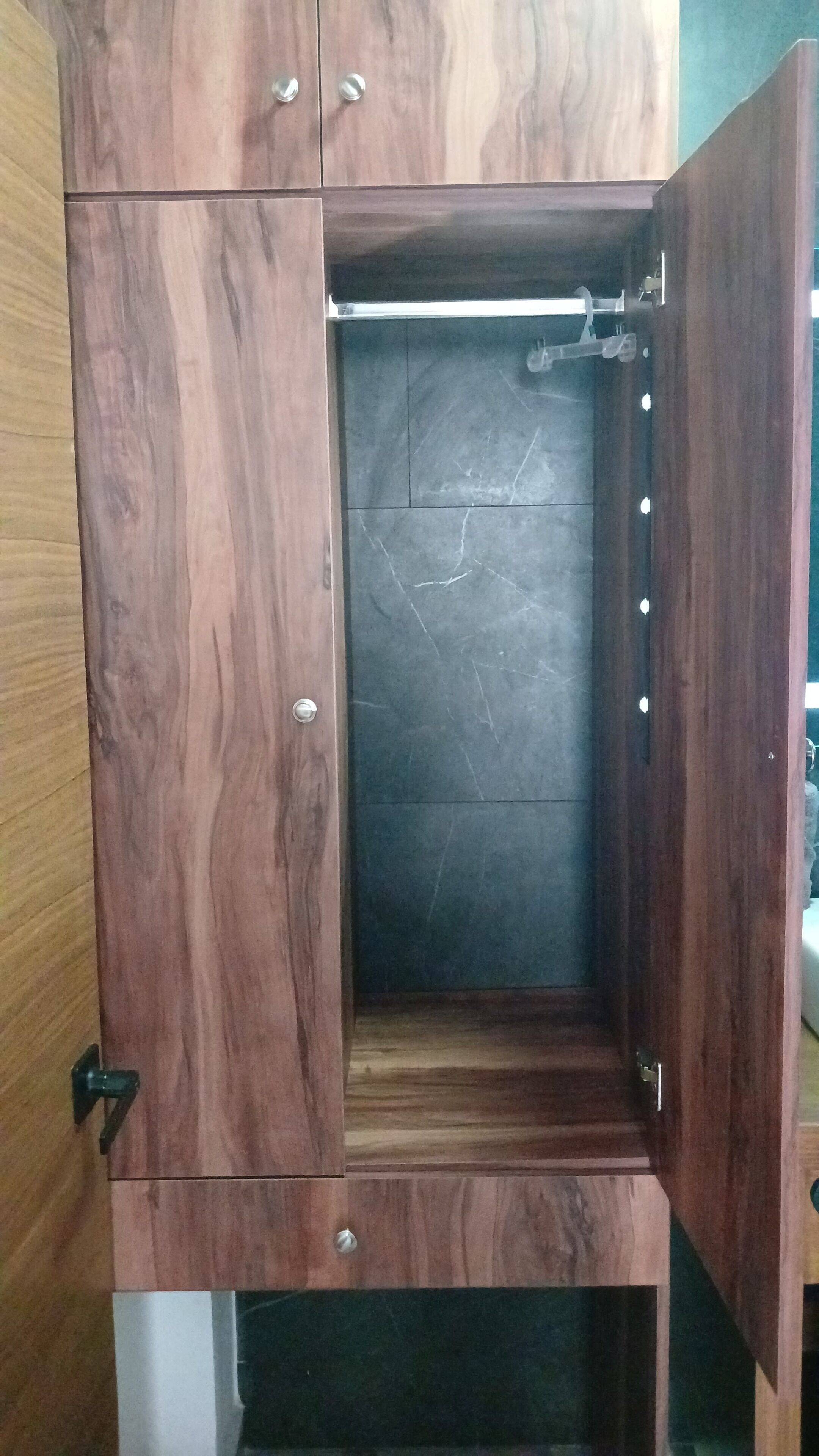 A wooden wardrobe with a marble interior, a hanging rod, and a small shelf.