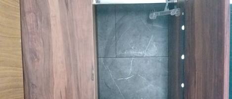 A wooden wardrobe with a marble interior, a hanging rod, and a small shelf.