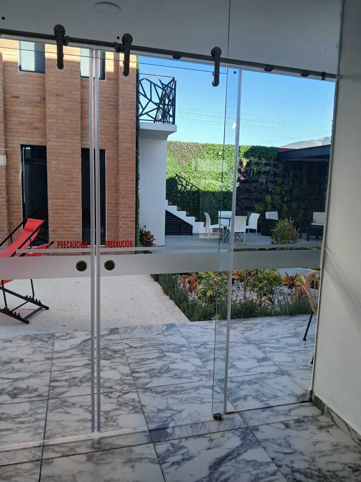 Un espacio exterior moderno con balaustrada de vidrio, pared de ladrillo y vista a un jardín ajardinado.