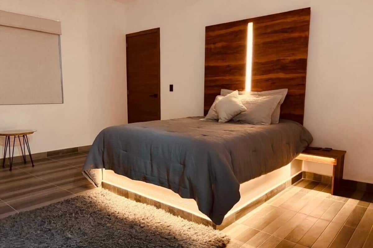 Quarto moderno com cama grande, mesa de cabeceira, luminária de chão e cabeceira de madeira.