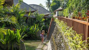 A pathway leading to a building with thatched roofs, surrounded by lush tropical vegetation. - Emana Bambooscape (Ubud)