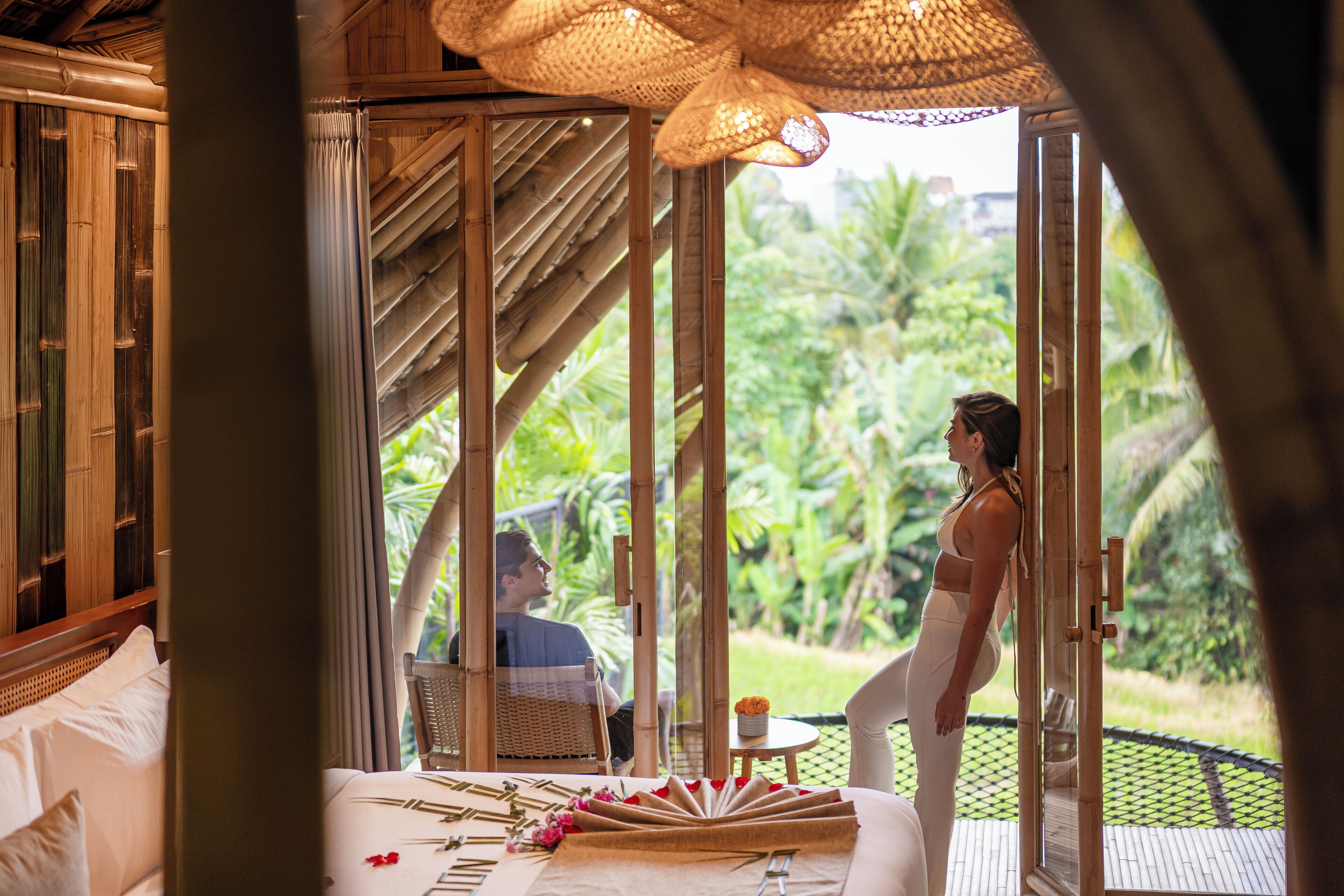 A room with a bed, a dining table, and a view of lush greenery.