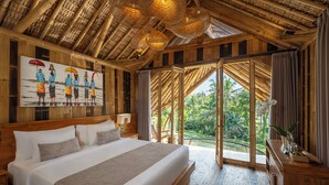 A large bed with white linens, a wooden headboard, and a painting of people holding umbrellas. - Emana Bambooscape (Ubud)