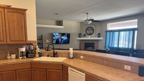 A modern kitchen with wooden cabinets, a dishwasher, a coffee maker, and a TV in the background. - Ridgeline Oasis! (Bullhead City)