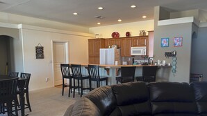 A modern living room with a black leather sofa, a dining area with wooden chairs, and a kitchen with wooden cabinets and a white refrigerator. - Ridgeline Oasis! (Bullhead City)