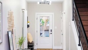 A hallway with a white door, a small bench, a framed picture, and a plant.