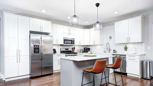 A modern kitchen with white cabinetry, stainless steel appliances, a central island with bar stools, and pendant lighting.