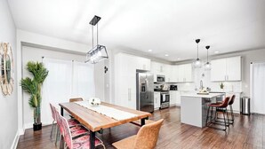 A modern kitchen with white cabinets, stainless steel appliances, and a wooden dining table with chairs.